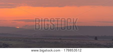 Sunset over Dartmoor National Park. Last moments of setting sun over Dartmoor Forest on misty evening in National Park in Devon England UK