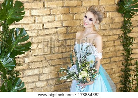 Bride in a beautiful turquoise dress in anticipation of wedding. Blonde in lace dress sea green with a bouquet . Happy bride emotion joy on her face. Beautiful makeup manicures and hairstyles women