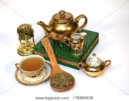 Golden tea set with a spoon full of herbs on white background