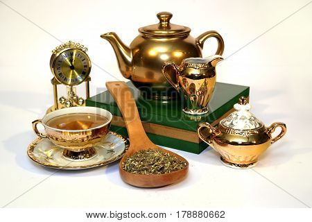 Golden tea set with a spoon full of herbs on white background