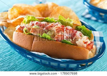 A delicious lobster roll with lettuce celery mayonnaise and potato chips.