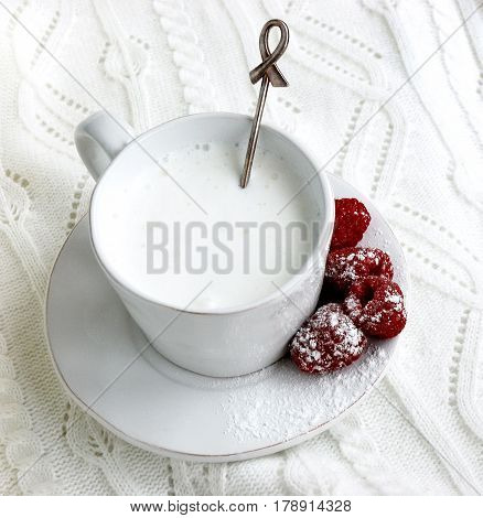 White Cup with milk and raspberries on a white background. Still life with white Cup and saucer with milk and raspberries.