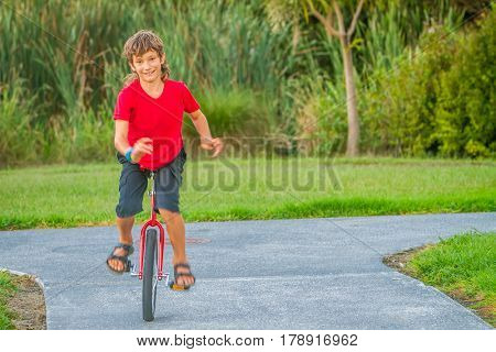 outdoor portrait of young boy riding a unicycle (one wheel bike) on natural background