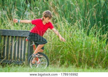 outdoor portrait of young boy riding a unicycle (one wheel bike) on natural background