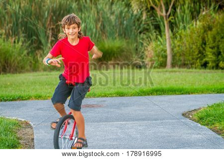 outdoor portrait of young boy riding a unicycle (one wheel bike) on natural background