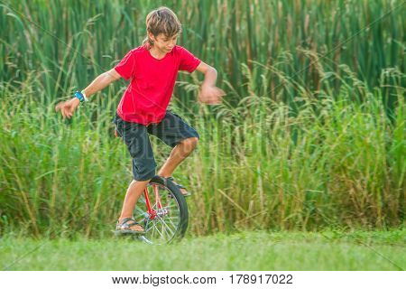outdoor portrait of young boy riding a unicycle (one wheel bike) on natural background