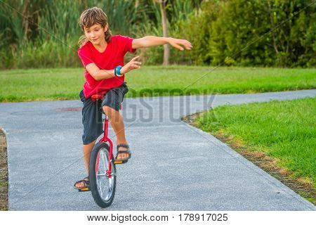 outdoor portrait of young boy riding a unicycle (one wheel bike) on natural background
