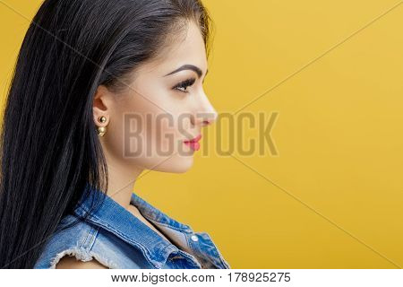 portrait of attractive young brunette woman in a denim vest on a yellow background.