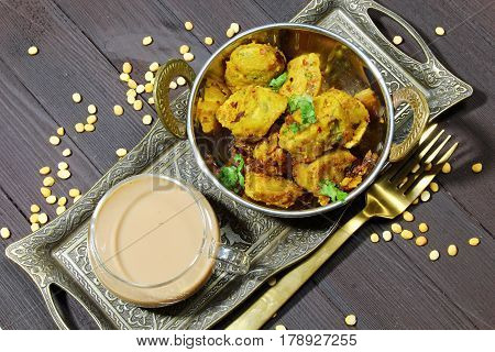 Overhead view of dry Gatte ki sabji or Dhoka made of chickpea flour or Besan with onions and ginger and other Indian spices and a cup of tea on a metal tray on blue wooden background.
