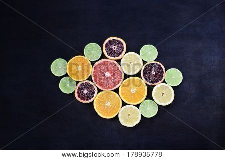 Variety of citrus fruits (orange blood oranges lemons grapefruits and limes) over a black rustic background. Image shot from overhead.