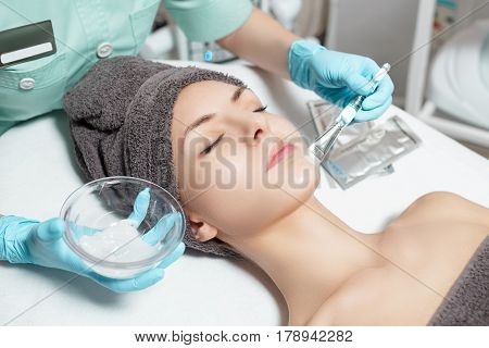 beautician applies face mask with a brush to the beautiful young woman in Spa salon. cosmetic procedure skin care. Microdermabrasion