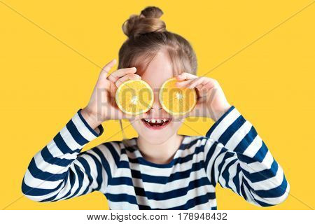 A girl with oranges on a background in the studio closes her eyes and laughs
