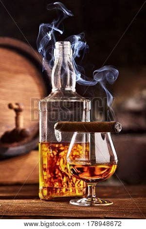 Glass of cognac or brandy with smoking cigar on wooden table