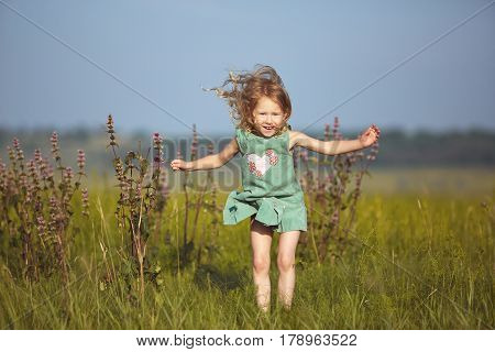 happy smiling girl in the field at sunny summer morning. girl in green dress Collects a bouquet of wildflowers and Jumping over the field cheerfully. The family travels, the children happily ran around the field