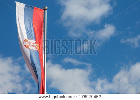 Photo of the official flag of the republic of Serbia with a backround of blue sky and clouds