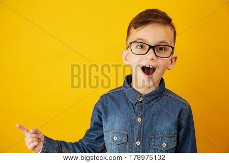A little boy shows his finger to the side against the yellowbackground