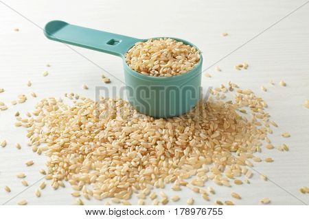 Full measure scoop and heap of brown rice on white background