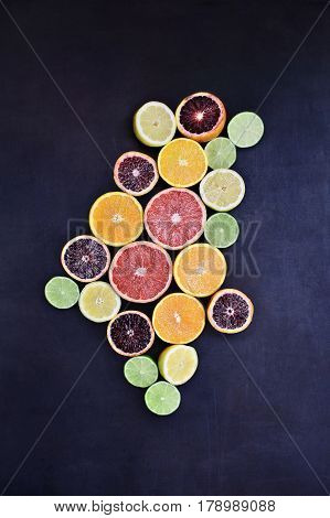 Variety of citrus fruits (orange blood oranges lemons grapefruits and limes) over a black rustic background. Image shot from overhead.