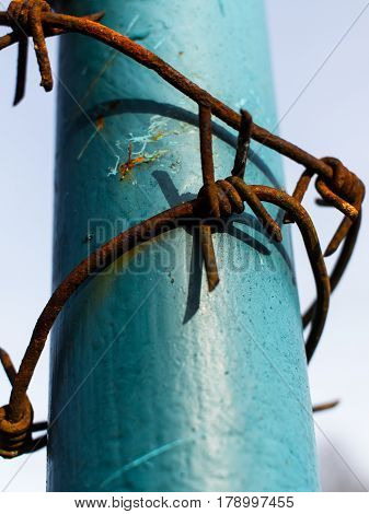 Old rusty barbed wire coiled around painted steel pipe pillar fence