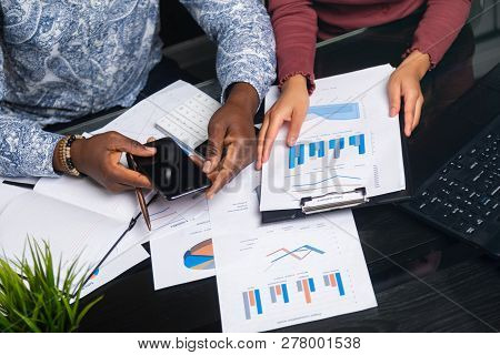 Hands Of Black People Holding Mobile Phone On Background Of Financial Documents In Business Space Cl