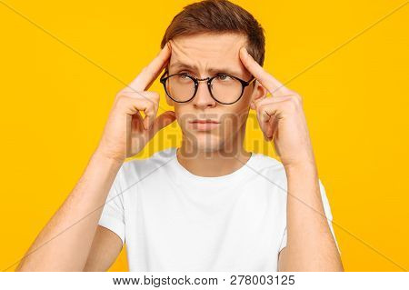 Portrait Of A Thoughtful Dreamy Guy With Glasses And A White T-shirt, Imagines Something In Mind, On