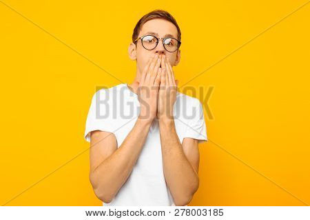 Portrait Of A Scared Man With Glasses, Guy Covering His Mouth With His Hands For Fear, On A Yellow B