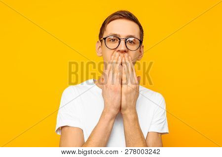 Portrait Of A Scared Man With Glasses, Guy Covering His Mouth With His Hands For Fear, On A Yellow B