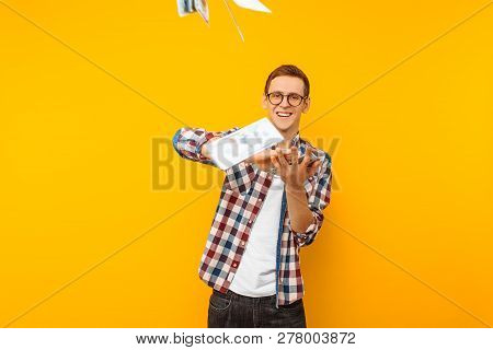 Happy Man, Wearing Glasses And A Plaid Shirt, Throwing Out Money Banknotes On A Yellow Background