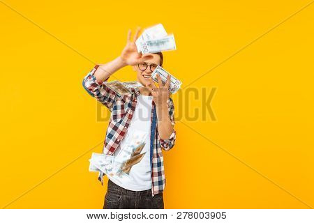 Happy Man, Wearing Glasses And A Plaid Shirt, Throwing Out Money Banknotes On A Yellow Background