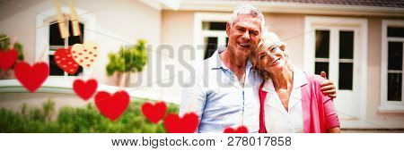 Hearts hanging on a line against senior couple with arms around standing in yard 