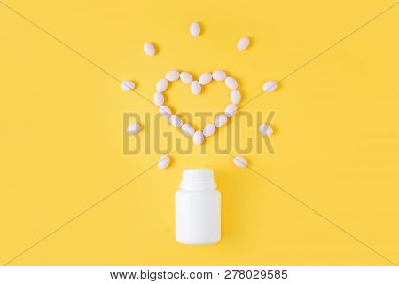 Pills In Shape Of Heart Dropped From Bottle On Yellow Background. Flat Lay, Top View.