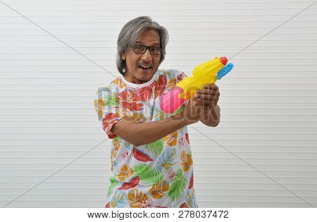 Happy Elderly Traveler Asian Man Wearing Summer Shirt And Glasses Holding Colorful Water Gun Over Wh