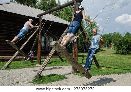 Talczy, Irkutskaya Oblast, Russia - 7 August 2017, Four People On A Wooden Swing Near The Tree And O