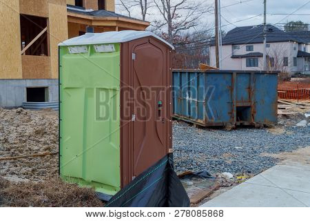 Portable Restroom On A Dumpsters Being Full With Garbage House Under Construction.