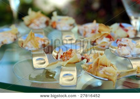 Gourmet banquet table featuring chicken and pasta canapÃÂ©s in individual serving spoons.