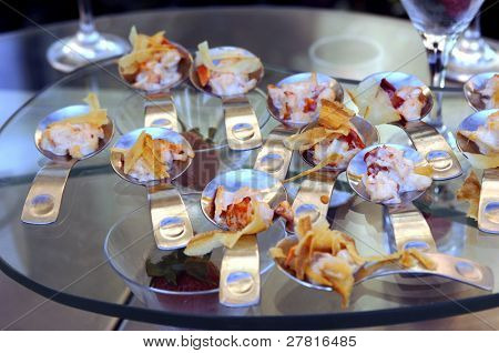 Gourmet banquet table featuring chicken and pasta canapÃÂ©s in individual serving spoons.