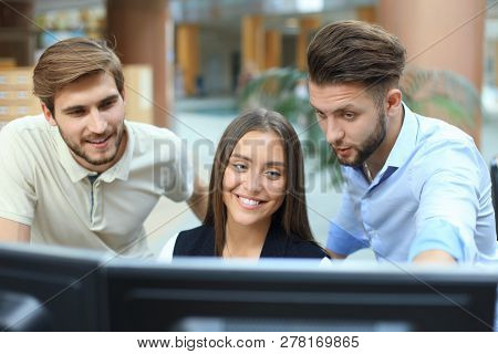 Group Of Young People In Casual Wear Sitting At The Office Desk And Discussing Something While Looki