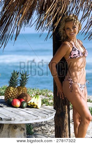 Ragazza bionda sexy del bikini in spiaggia in bikini rosa e marrone di Swimbay sotto un ombrello palapus w