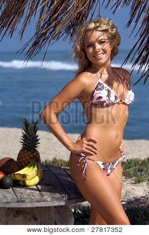 Ragazza bionda sexy del bikini in spiaggia in bikini rosa e marrone di Swimbay sotto un ombrello palapus w