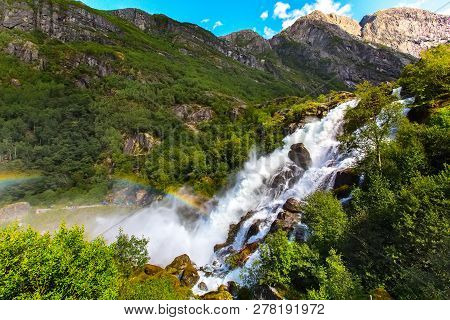 Waterfall And Rainbow On The Way To Briksdal Or Briksdalsbreen Glacier In Olden, Norway And Green Mo