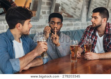 Man Talking On Phone And Asking For Silence, Sitting In Bar With Friends