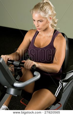 Krásná blonďatá žena během cardio cvičení na ležící rotoped v tělocvičně