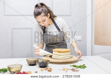 Confectioner With Pastry Bag Squeezing Cream On Cake At Kitchen. The Concept Of Homemade Pastry, Coo