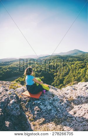 A Woman Is Sitting In A Sleeping Bag At Sunset. Camping On Top Of A Mountain. A Smiling Girl Rests A