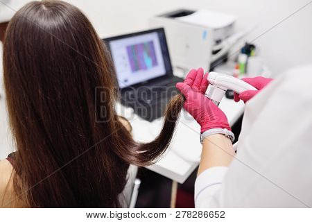 Doctor Dermatologist Diagnoses The Structure Of The Hair Of A Young Pretty Girl With A Special Tool 