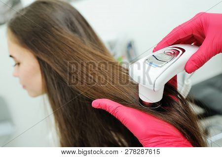 Doctor Dermatologist Diagnoses The Structure Of The Hair Of A Young Pretty Girl With A Special Tool 