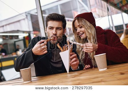 Close-up Of Young Couple Are Eating Churros At The Street Food Market.
