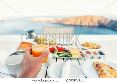 Luxury travel resort breakfast in room service at fancy hotel restaurant with amazing balcony view over Santorini island, Oia, Greece. Europe vacation food selfie. Man drinking morning orange juice.