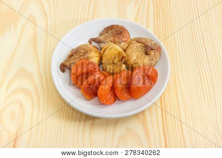 Dried Fig Fruits And Dried Apricots On The White Saucer On Light Colored Wooden Surface