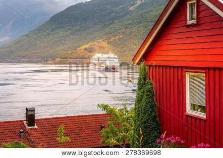 Flam, Norway - July 31, 2018: Norwegian Fjord Sognefjord Landscape, Red Wooden House And Aidaluna Cr